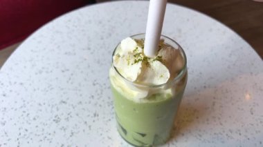 Frappuccino ile dondurma ve kremalı Matcha çayı yeşil arka planda cam bardakta. Yanında da bir kase Matcha dondurması..