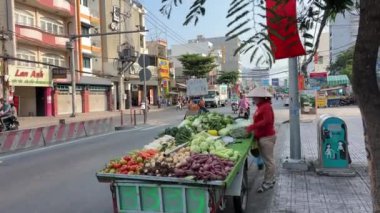 Vietnam caddesinde oturan kadın, yol kenarındaki bir tezgahtan taze sebze satıyor. Motosikletli, şapkalı, Vietnamlı, müşteri bekleyen yetişkin bir kadın. Ho Chi Minh Şehri Vietnam 09.30. 2024