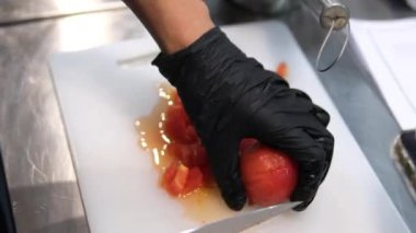 Soyulmuş domatesleri kare şeklinde kesin. Siyah lateks eldivenli büyük bıçaklı eller pişirin. Yüksek kalite 4k görüntü