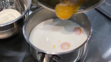 Süt, yumurtayla kaseye akıyor, ağır çekimde. Hamur hazırlığı. Şef cam bir kaseye süt döker. Süte sarısı ekle