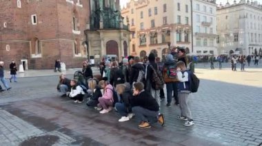 Çocuklar okul gezisinde Krakow tarihi pazar meydanı, Krakow, Polonya 11.06.2024 ile dışarıda bir konferans dinliyorlar.