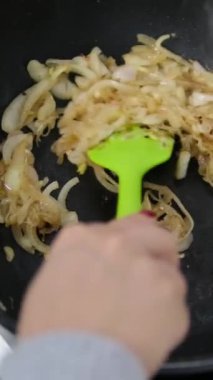 Çiğ soğanlar, rafine yağlı, sıcak, siyah bir tavada karamelize edilir ve ahşap bir spatulayla sürekli karıştırılır. Üst Manzara. Kapatın. 4 bin. Yüksek kalite 4k görüntü