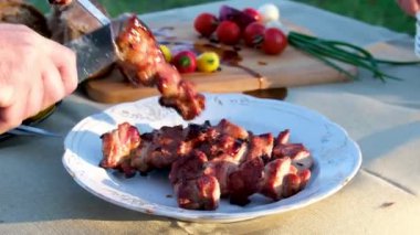 Açık havada mangal kömüründe şiş kebap. Adam pişirilmiş domuz barbeküsünü bıçakla şişten çıkartıyor. Şişi şişlemeden kaldır
