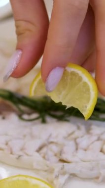 Şefin balığın üzerine yarım limon sıkıştırdığı yavaş çekim görüntüleri. Restoranda yeşil yapraklar ve bir dilim limonla servis edilen balık. Dikey videolar.