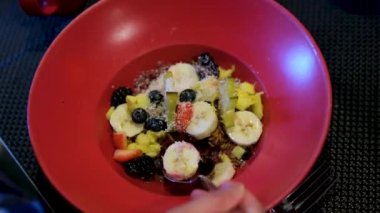 Acai kasesi, hindistan cevizi, muz, mango, ananas. Karanlık bir restoranda kırmızı tabak. Sağlıklı gıda meyveleri