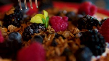 Karpuz, susam kreması, ev yapımı granola, donmuş böğürtlen, tofu kreması sağlıklı kahvaltılık ahududu ve karpuz yenilebilir çiçek restoranında böğürtlen. kırmızı tabakta servis ediliyor.