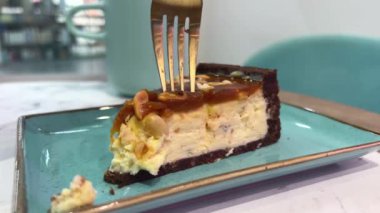 Fıstık Ezmeli Cheesecake ve kafede karamel. Mavi bir tabakta altın çatalla turkuaz kaplamalı lezzetli bir pasta kırıyorlar. Yüksek kalite 4k görüntü