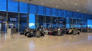 Uçağı bekleyenler, kafelerde ve karanlık pencerelerin yanındaki koltuklarda oturarak U 31 32 Barselona Havaalanı 11: 03.2024 sayılı Barselona İspanya uçağını bekliyorlar.