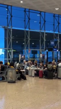 Uçağı bekleyenler, kafelerde ve karanlık pencerelerin yanındaki koltuklarda oturarak U 31 32 Barselona Havaalanı 11: 03.2024 sayılı Barselona İspanya uçağını bekliyorlar.