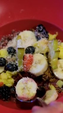 Acai kasesi, hindistan cevizi, muz, mango, ananas. Karanlık bir restoranda kırmızı tabak. Sağlıklı gıda meyveleri