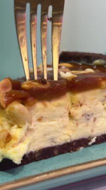 Fıstık Ezmeli Cheesecake ve kafede karamel. Mavi bir tabakta altın çatalla turkuaz kaplamalı lezzetli bir pasta kırıyorlar. Yüksek kalite 4k görüntü