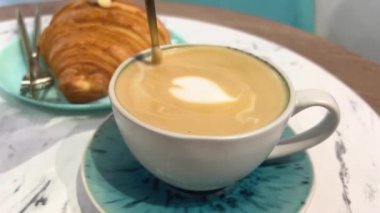 Hoş bir kafede cappuccino servisi yapan bir kadının yakın çekimi. Bir kafede taze çiçeklerle vurulmuş ve kahve servisi yapan ve kruvasan yiyen bir kadın. Sessiz bir kafede lezzetli bir kahvaltı. Ay çöreği kapuçinosu.