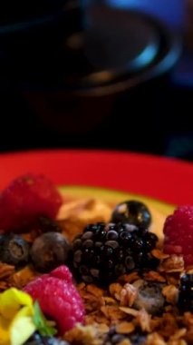 Karpuz, susam kreması, ev yapımı granola, donmuş böğürtlen, tofu kreması sağlıklı kahvaltılık ahududu ve karpuz yenilebilir çiçek restoranında böğürtlen. kırmızı tabakta servis ediliyor.