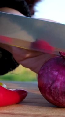 Eller kırmızı soğanı tahta tahtada bıçakla kesiyor, yakın plan. Doğada mangal için kesilmiş farklı sebzeler.