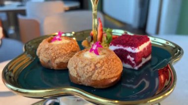 Yüzüklü mini choux hamur işleri kızı maket tabağından, sepet ve kırmızı kadife kekin yanındaki yenilebilir çiçekli pastaları alır. Yüksek kalite 4k görüntü