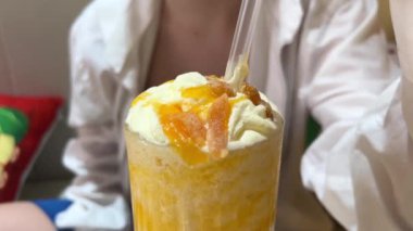  Taze mango dilimleri ve siyah pipetle kaplı, uzun bir bardakta servis edilen canlı ve kremalı bir mango kokteyli. Yaz atmosferi için mükemmel bir tropikal içecek. Yüksek kalite 4k görüntü