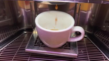 Kahve makinesi bardağı dolduruyor. Kahve makinesiyle kahve yapıp fincana koymak, otomatik kahve makinesinden çıkan espresso kahvesi. İçecek içeceği. Leylak pembesi kadınlar bardağı.