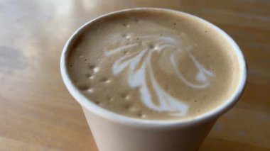 Küçük seramik bardak taze demlenmiş kapuçino, süt köpüğünde kalp resmi, çay kaşığıyla dikkatlice kaldıran bir kadın. Müşterileri Bali Adası 'ndaki kafeteryaya çekmek için kullanılan son moda latte sanatı..