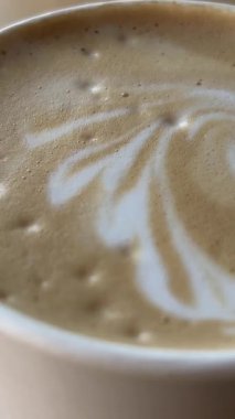 Küçük seramik bardak taze demlenmiş kapuçino, süt köpüğünde kalp resmi, çay kaşığıyla dikkatlice kaldıran bir kadın. Müşterileri Bali Adası 'ndaki kafeteryaya çekmek için kullanılan son moda latte sanatı..