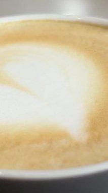 Masada kalp şeklinde köpük olan kapuçino. Kahve fincanında sanat Latte 'si. Lezzetli taze kapuçino. Güzel latte sanatıyla cappuccinonun tadını çıkarıyor. Yüksek kalite 4k görüntü