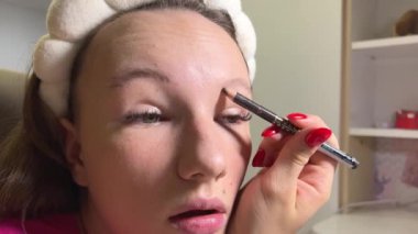 Genç, açık tenli bir kız kaşlarını boyuyor. Geniş kaşlar. Doğal güzellik. Mükemmel hafif makyaj. İnce pembe dudaklar. Aynadaki yansıma. Kaşlara jöle. Yüksek kalite 4k görüntü