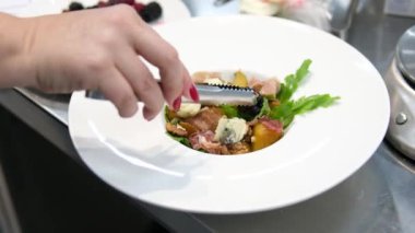 Şefin elleri kırmızı üzümlü sağlıklı sebze salatası servis ediyor. Tabak servisi. Yemek pişirme süreci. Sağlıklı bir yaşam tarzı. Yakın plan. Mavi peynir ve jambon