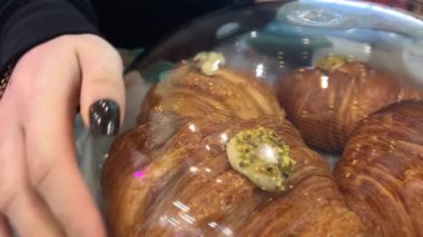 Taze hamur işi almak için kruvasan satan bir dükkan. Müşteri dikkatli bir şekilde taze hamur işleri ve taze kruvasanları tezgahtan alır. Dükkanda taze kruvasanlar var.. 