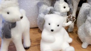 Beyaz kutup hayvanları arasında sıcacık giyinmiş küçük bir ayı figürünün yer aldığı, neşeli bir tatil oyuncağı gösterisi, tuhaf bir kış sahnesini çağrıştırıyor. Yüksek kalite 4k görüntü