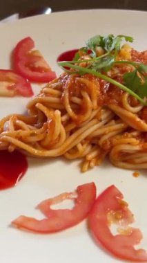 Beyaz bir masada servis edilen fesleğen ve maydanozla süslenmiş zengin domates soslu spagetti makarna tabağının üst görüntüsü. Yüksek kalite 4k görüntü