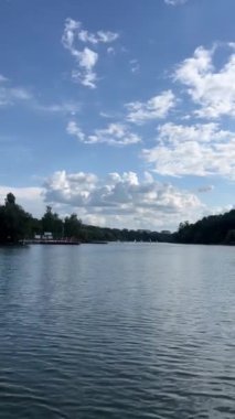 Hava aracı, bulutlu bir gökyüzü altında sakin suları kesen bir yelkenlinin yer aldığı sakin bir göl sahnesini yakalar. Yansıtıcı yüzey ve uzak ufuk barışçıl bir doğa görüşü yaratır..