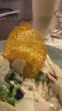 Tavuklu Sezar salatası, marul, vişneli domates, parmesan peyniri, pizza ve kafedeki ahşap masada bir fincan kahve. Arka planda bulanık bir siluet var. 