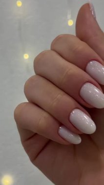 Güzel yeni yıl beyaz oval manikürü beyaz bir çelenk duvarının arka planında. Güzellik salonu, manikürcü, genç bayan eli. Yüksek kalite 4k görüntü