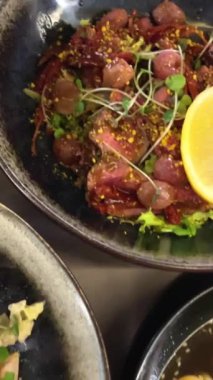 Biftekli salata, barbekü üzümü, Sezar salatası, marul, barbekü hindisi, pastırma ve ton balığı sosu. Erişteli ramen çorbası udon yumurtaları yeşil soğan soya sosu siyah tabakta susam