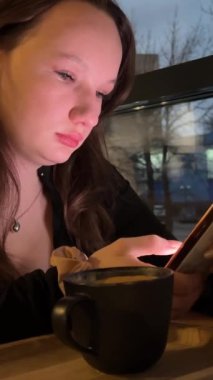 Kafede akıllı telefon kullanan güzel bir genç kız sosyal medyada mesajlarını paylaşıyor kahve dükkanında mobil teknolojinin keyfini çıkarıyor. Yüksek kalite 4k görüntü