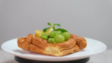 Konserve şeftali, siyah üzüm ve yeşil nane şekerleriyle süslenmiş nefis ev yapımı şeftalili cheesecake manzarası ahşap masada dönüyor. Yüksek kalite 8K görüntü
