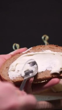 Parlak bir mutfakta aşçı kızarmış ekmeğe yumuşak Philadelphia peyniri sürer. Parlak bir mutfakta kadınların elleri kızarmış tostun üzerine yumuşak peynir ve tereyağı sürüyor. Yavaş çekimde yakın çekim, renkli.