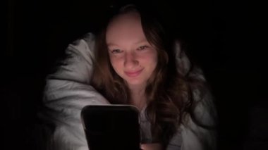Genç kız gece yatakta yatarken akıllı telefon kullanıyor, sosyal medyayı karıştırıyor ve mesajlaşıyor. Sağlıklı uyku değil. Uykusuzluk ve yatmadan önce akıllı telefonun verdiği zarar. Sosyal ağlara bağımlılık