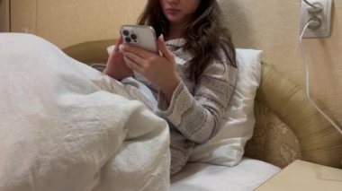 Üzücü üzgün, tatminsiz, beyaz tişörtlü, evde pijama giyen, yatak odasında uzanan, cep telefonlu, mutsuz bir kadın. Kötü ruh hali yaşam tarzı konsepti