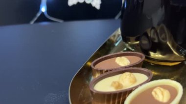 Altın tepside düzenlenmiş renkli, el yapımı çikolata ve şekerlerden oluşan canlı bir karışım. Çeşitlilikte her biri benzersiz şekil ve dokulara sahip kırmızı, yeşil ve koyu çikolatalar yer almaktadır. 