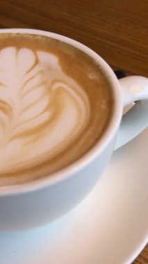Üzerinde güzel bir barmen deseni olan sıcak kahve fincanı ahşap masa bükülmüş elinde beyaz kahve, sütlü beyaz tabaklar, kafein. Yüksek kalite 4k görüntü