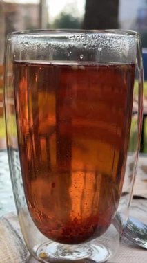 Sıcak çay, cam sürahiden şeffaf çift duvarlı bardağa dökülüyor, buhar yükseliyor, sıcak ortam ışıklarıyla çekiliyor. Duble duvar bardağı. Çift katlı çay.