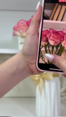Cep telefonlu kadınların elleri ve beyaz manikürlü çiçeklerin videosunu çek. Odada, sosyal ağlar için sevilen birinin güzel bir buket hediyesinin videosu var. Yüksek kalite 4k
