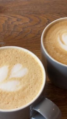 İki fincan latte cappuccino bembeyaz, güzel desenli, ahşap bir masa kafeteryasında arkadaşlarıyla yürüyüş yapan el, diğeriyle tokuşturur.