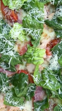 Ahşap masada parmesan peynirli leziz pizza Sezar 'ı sos dökerken. Bitkisel pizza. Marul, domates, peynir.
