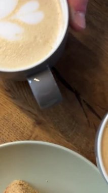 Tahta bir masa üzerinde güzel bir kahvaltı kahve ve kekler kruvasan sabah el hareket ettirme fincan garsonu kahve aromatik tatlı kek getiriyor latte cappuccino Düz Beyaz. Yüksek kalite 4k