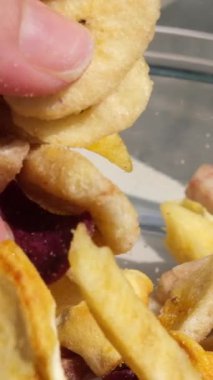 Ahşap bir yüzeyde kurumuş egzotik meyve dilimleri yığını. Makro. Dolly vurdu. Vitamin atıştırmalığı. Farklı kurumuş meyve parçaları muz tatlı patates anananası cam bir tabağa dökülüyor.