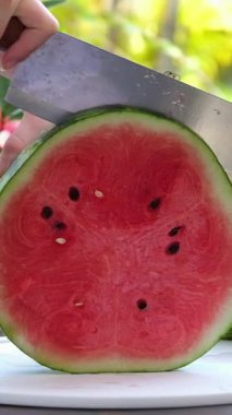 Altın saat boyunca açık havada canlı yeşil kabuklu sulu kırmızı karpuz dilimleyen el yapımı taze, olgun karpuz, yumuşak doğayla çevrili, tabakta parçalara ayrılıyor. Yüksek kalite 4k