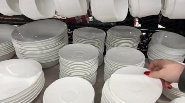 Porselen fabrikası, raflarda bardak ve tabak üretimi. Birçok küçük tabak, seramik kil tarafından yapılmış yuvarlak şekilli. Toprak donanımı üretimi. Mağazadan yemek seçmek.