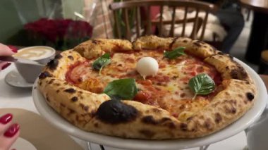 Margherita pizzalı, mozarella domatesli fesleğen bir restoranda duruyor. Dilimlenmiş yemek, yemek, çiçekler, kahve, romantizm, kadın eli kırmızı manikür olacak. Yüksek kalite 4k