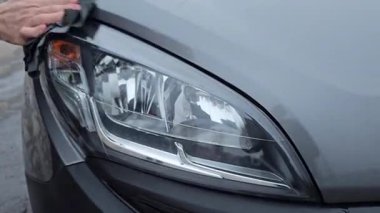 Bir adam gri bir arabanın farına bir bez parçası siler. Yüksek kalite 4k görüntü